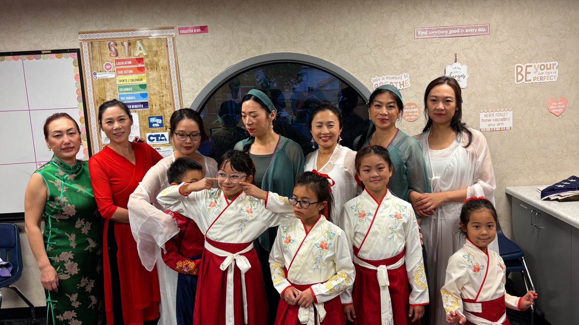 Group photo of SCV Chinese Dance performers backstage, featuring women in traditional Chinese dresses and young girls in matching red and white outfits after their performance at James Foster Elementary.